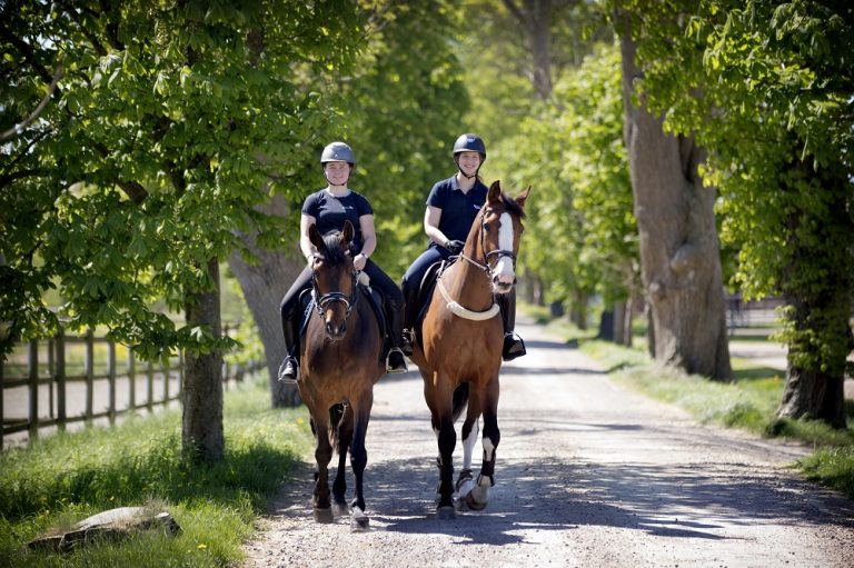 Två elever som rider på anläggningen på väg till lektion.