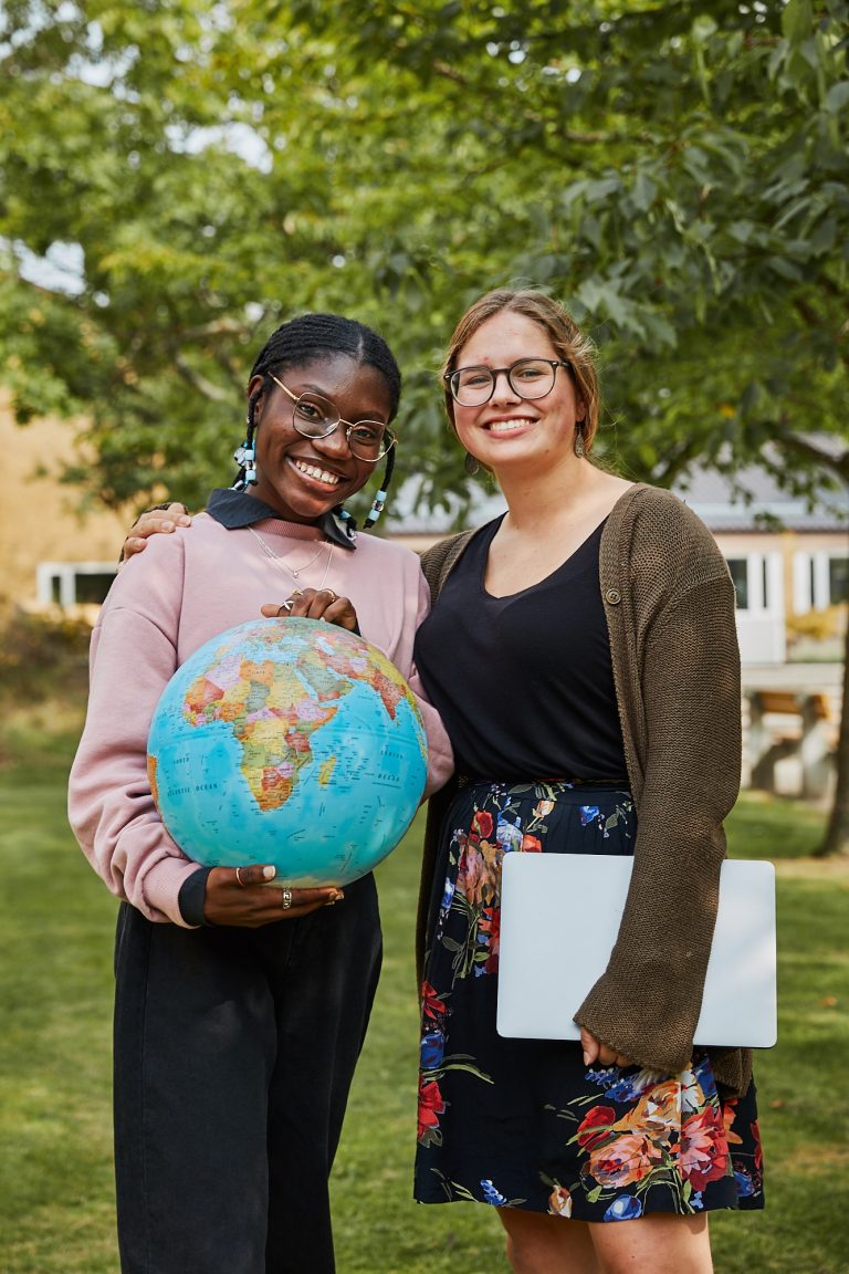 Two happy students standing outside on a lawn holding a globe.