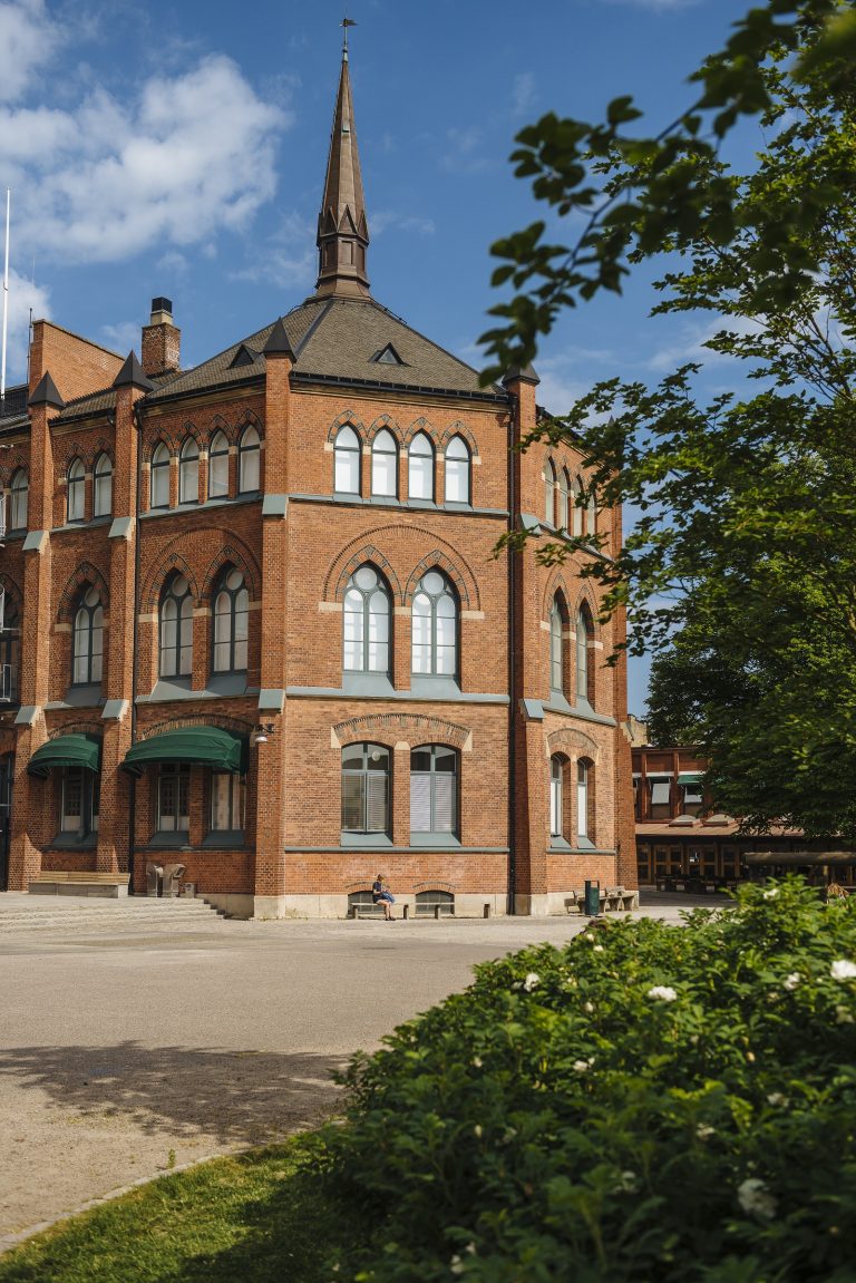 Katedralskolans huvudbyggnad sedd från sydväst. Träd i förgrunden och blå himmel.