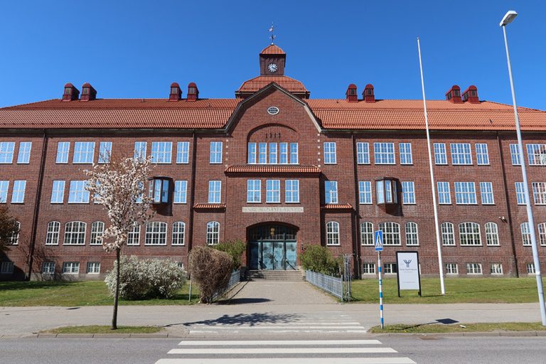 Stor röd tegelbyggnad i soligt väder med blå himmel. 