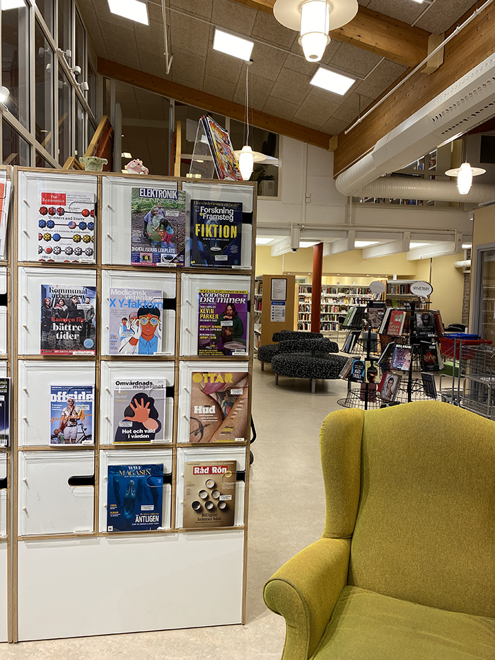 Gul fåtölj och tidningar i ett tidningsställ på skolbibliotek som finns på Ystad Gymnasium.