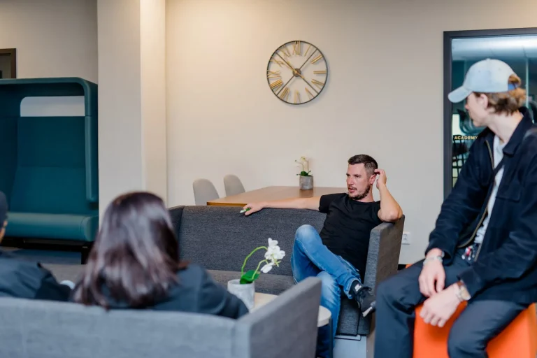 Två elever sitter i en soffgrupp och pratar med en lärare på skolan.