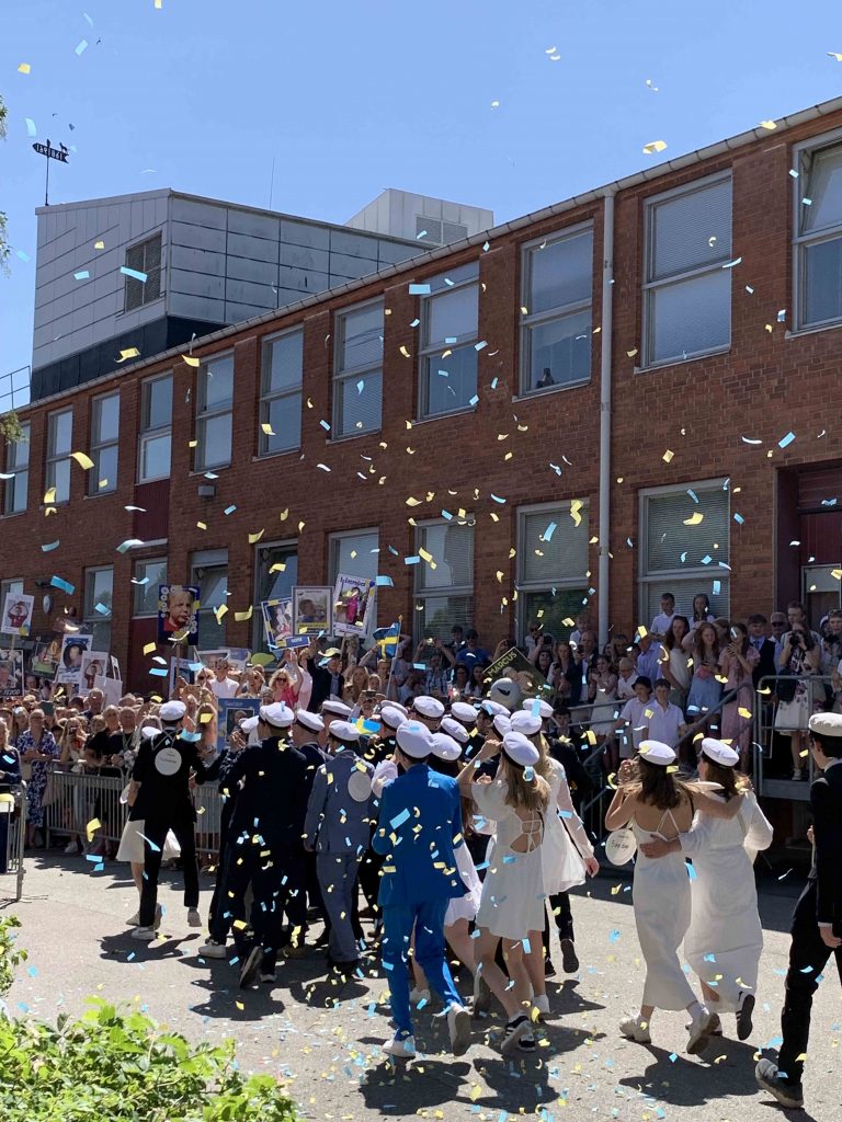 Elever iförda studentmössor och fina kläder på skolgården där deras familj och vänner väntar på att gratulera dem.