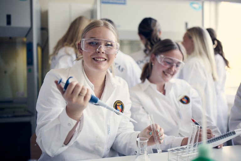 Glada elever iklädda labbrockar och skyddsglasögon utför laborationer i skolans nya, ljusa och högutrustade labb. 