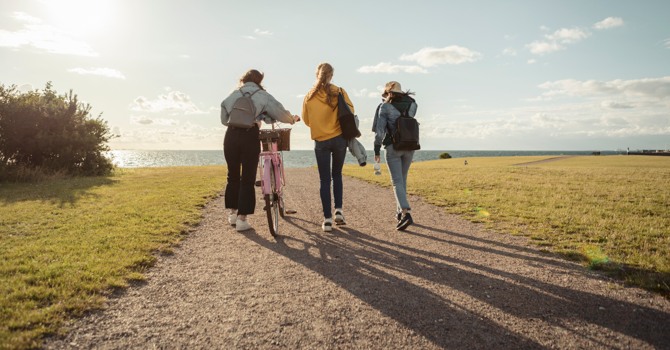 Tre ungdomar promenerar på en stig mot havet