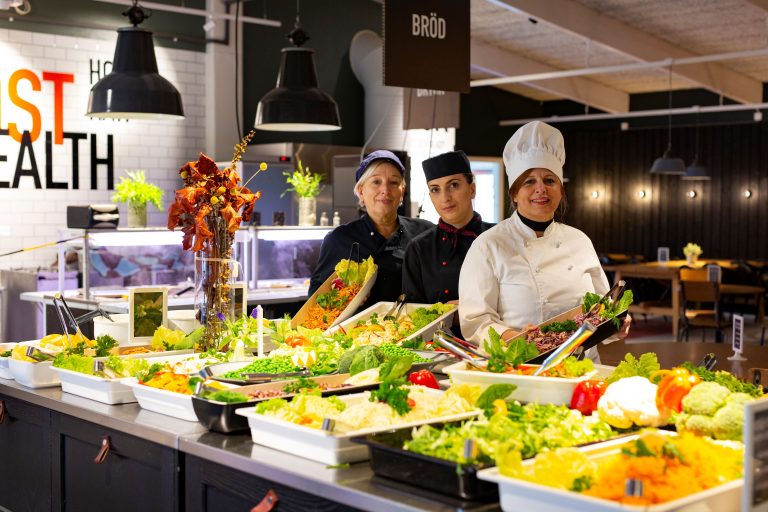 Tre personal i vår skolrestaurang står framför en färgsprakande salladsbuffé.