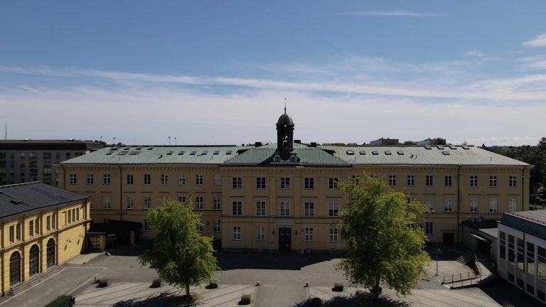 Stor gul skolbyggnad sedd uppifrån med två träd på skolgården.