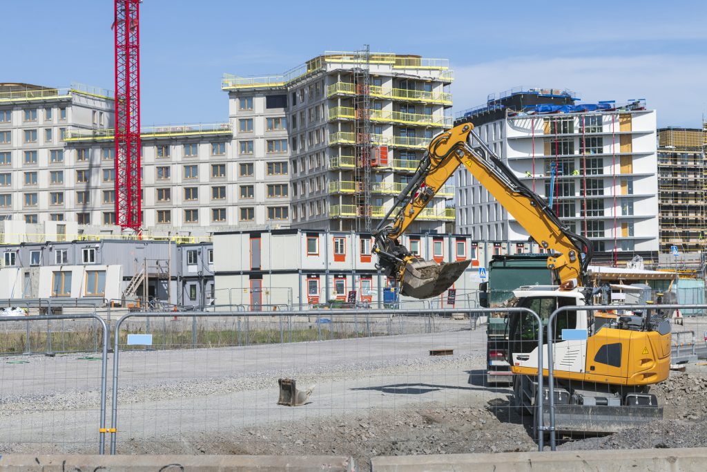 Grävskopa på byggarbetsplats med flerfamiljshus.