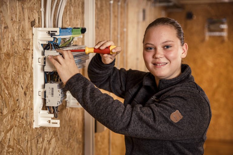 En glad tjej som är elev på elprogrammet som står och skruvar.