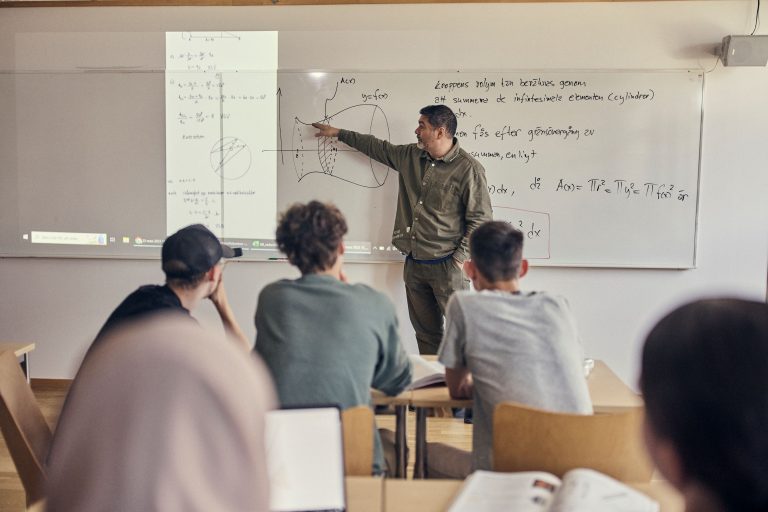 Matematikundervisning i klassrum. Lärare framme vid tavlan och elever som lyssnar.