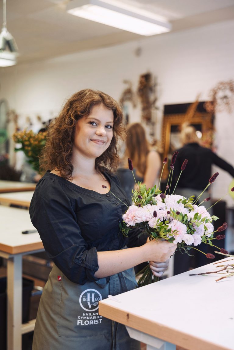 En floristelev visar sin nygjorda bukett i floristklassrummet.