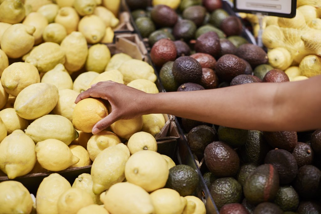 Hand som sträcker sig efter en citron i en fruktdisk med citroner och avocados.