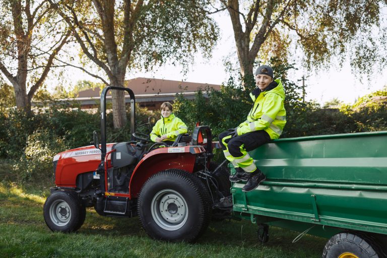 Två elever arbetar med traktor och släp i trädgårdsmiljö.