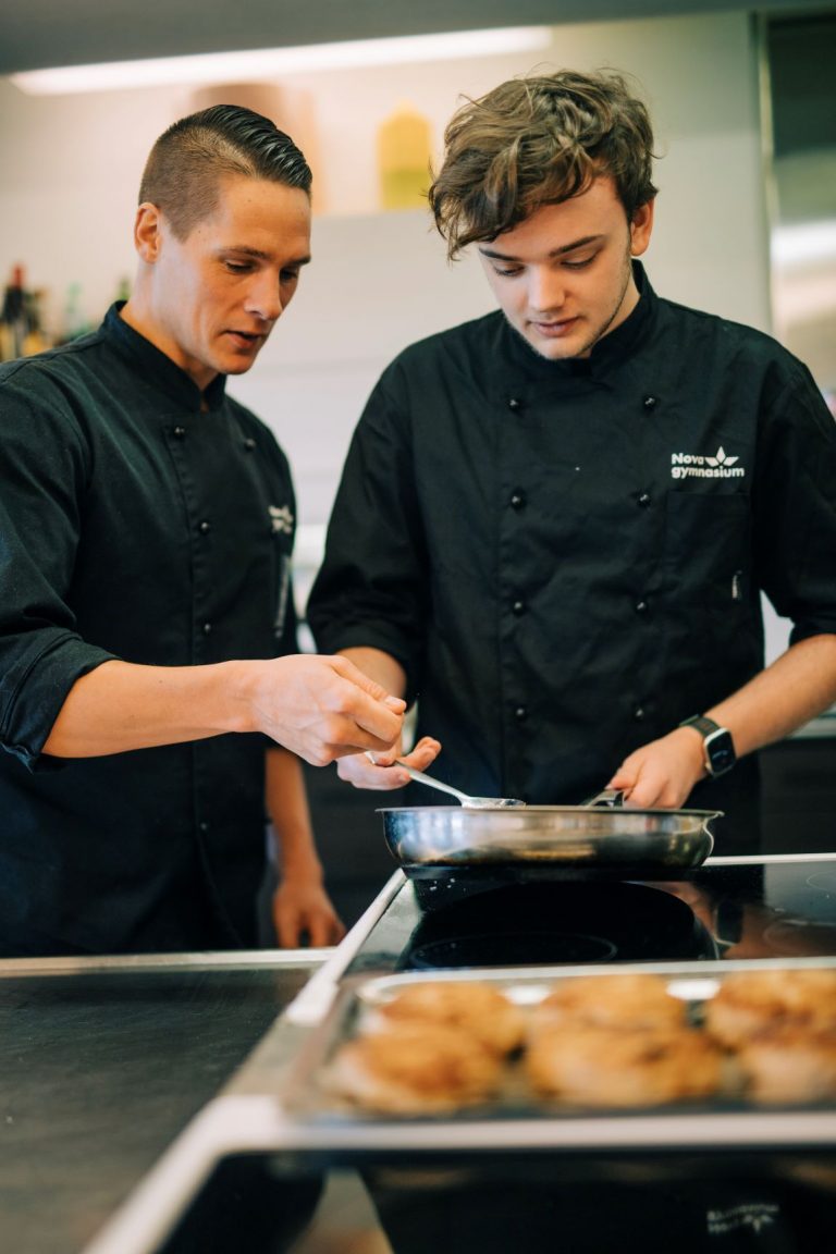 Lärare instruerar en elev som håller i en stekpanna på restaurang- och livsmedelsprogrammet. 