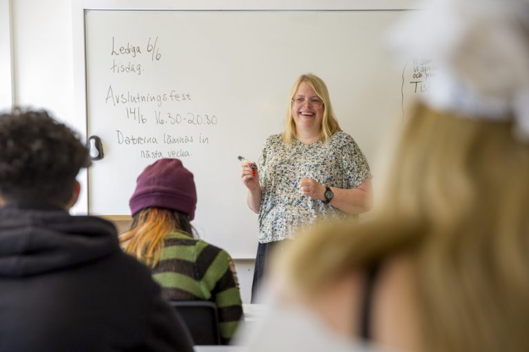 En glad lärare står framför klassen och undervisar.