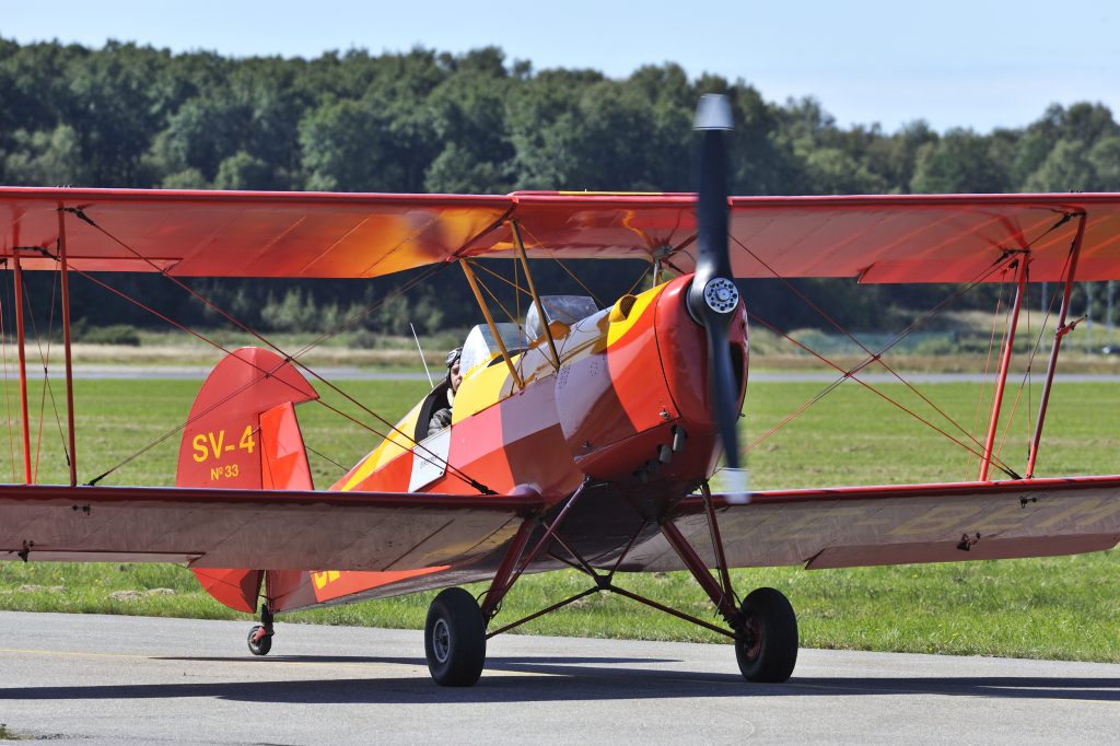 Litet rött propellerflygplan med gula detaljer på som står på startbanan.