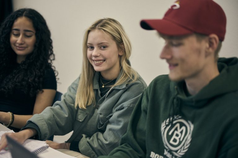 Tre glada elever sitter tillsammans i klassrumsmiljö.