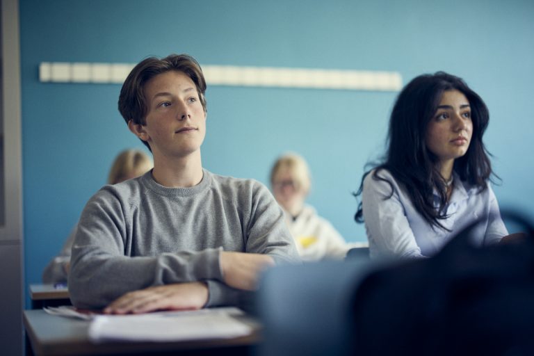 Några elever sitter i klassrumsmiljö och ser ut att delta i en lektion. 