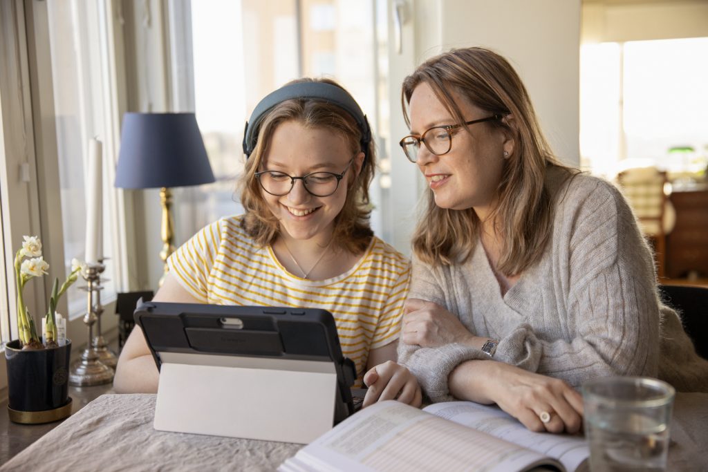 Mamma och dotter sitter tillsammans vid bordet och, med ett leende, tittar på en ipad.