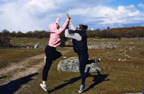 Två elever hoppar och gör en high-five utomhus. Gräs, stenar och blå himmel i bakgrunden.