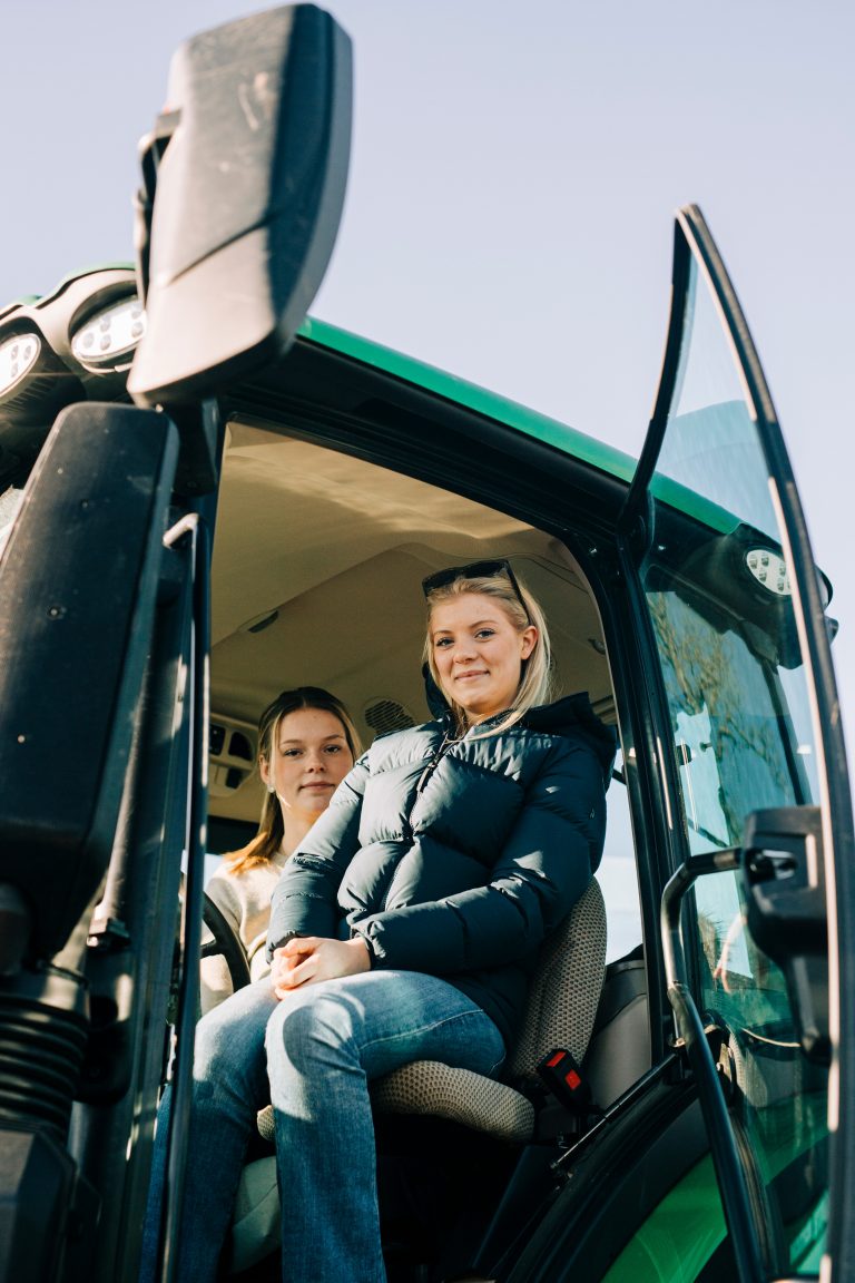 Två tjejer som sitter i en grön traktor.