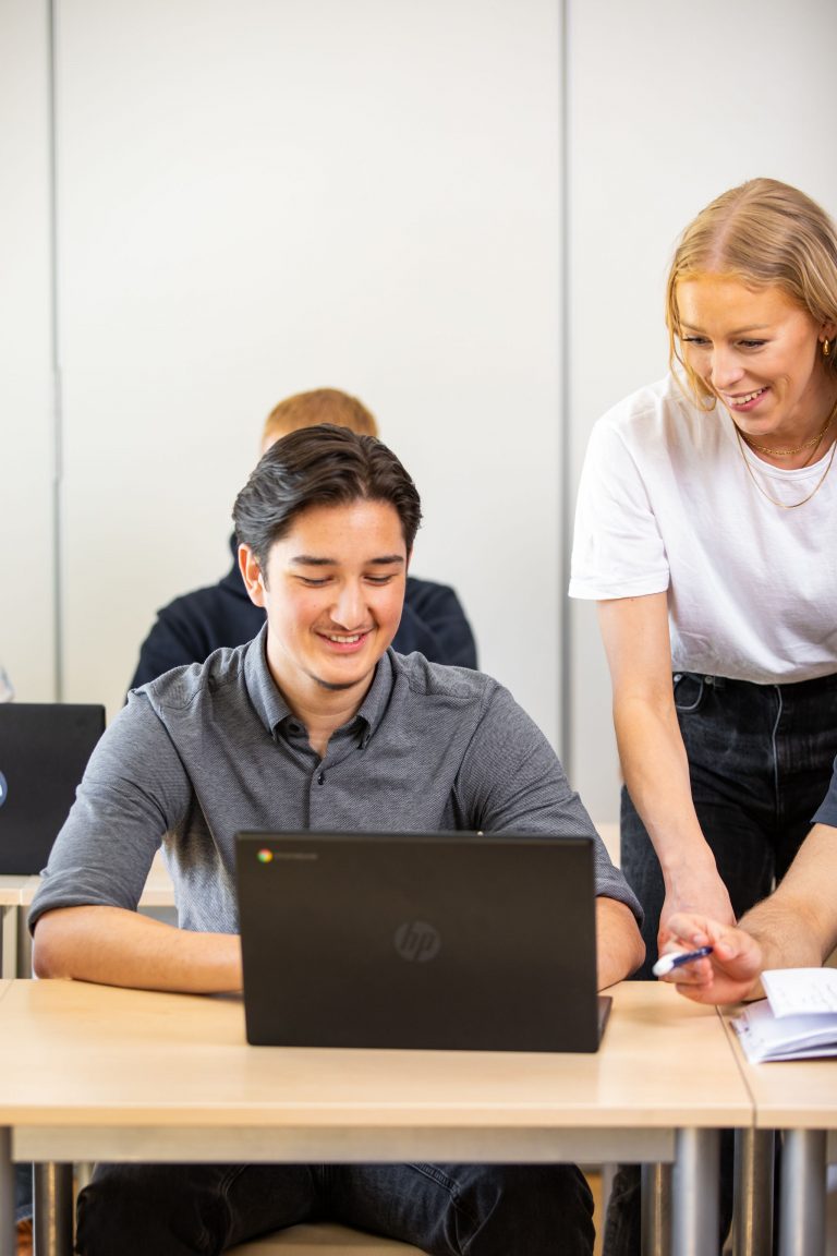 Lärare hjälper elever som sitter med laptop.