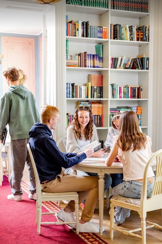 Fyra elever sitter och läser i skolans bibliotek. En elev står i bakgrunden.