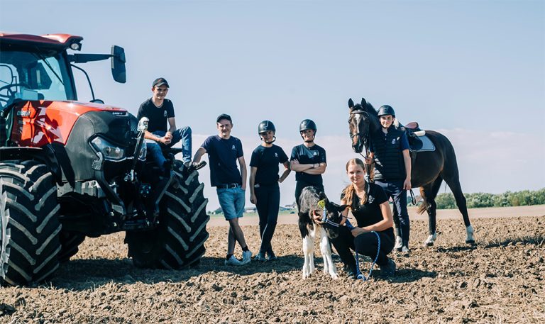 Elever träffas och pratar på åkern. En elev sitter på en traktor, en håller i en hund och en håller en häst. 