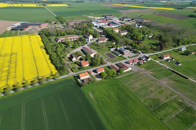 Drönarbild över Bollerups borg, slott, stall och fält i ett landskap av åkrar och alléer.