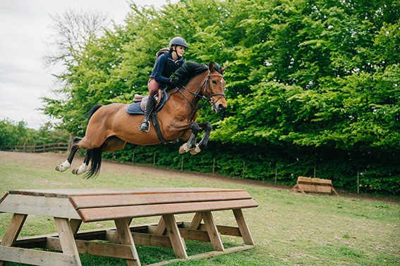 Elev som hoppar terränghinder på en av våra skolhästar.