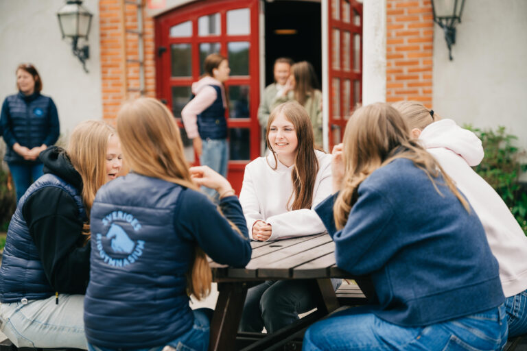 Glada elever som går ut ur och några som sitter framför skolbyggnaden.