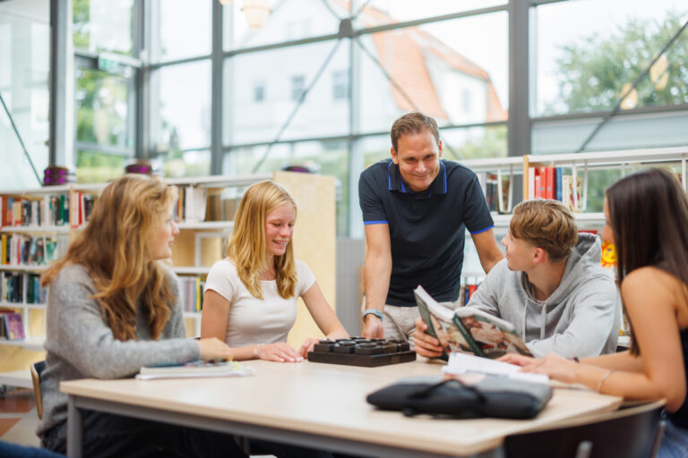 Elever diskuterar en uppgift med sin lärare i vårt bibliotek.