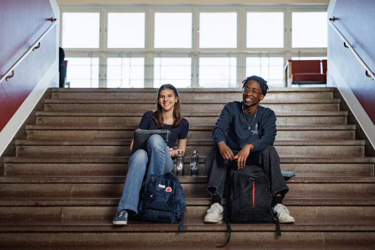 Two happy students sitting on the entrance stairs to the school.