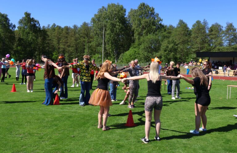 Flera elever håller i varandras händer, utomhus på en gräsmatta under en klasskampstävling.