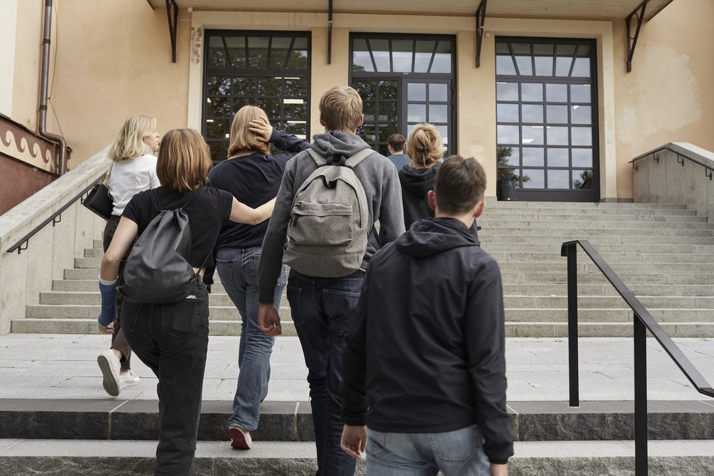 Flera elever går uppför en trappa mot entrén till en gymnasieskola.