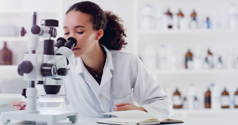 En elev står i ett laboratorium och tittar i ett mikroskop.