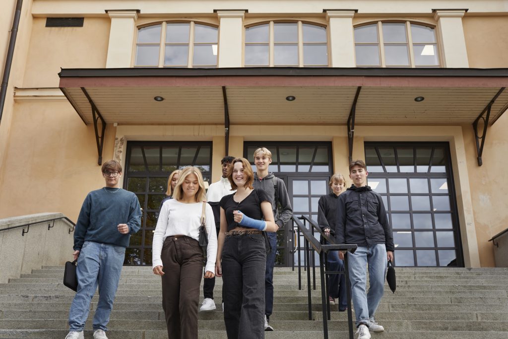 Ungdomar på väg nerför en trappa framför en skolbyggnad.